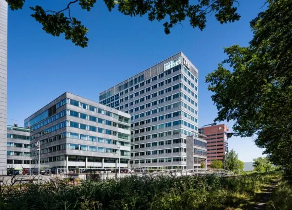 Kantoorcomplex aan de Thomas R. Malthusstraat met het Adam Smith Building, omgeven door groen en onder een heldere blauwe lucht.